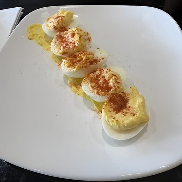 Five deviled egg halves with paprika and a yellow sauce on a white rectangular plate.