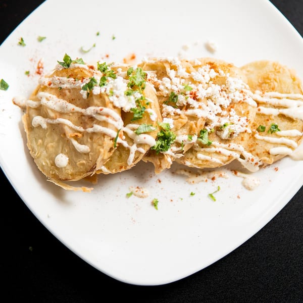 Three golden-fried plantain fritters topped with white cheese, cilantro, paprika, and a creamy sauce.