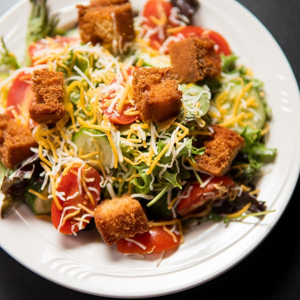A fresh garden salad with mixed greens, tomatoes, cucumbers, shredded cheese, and crispy croutons.