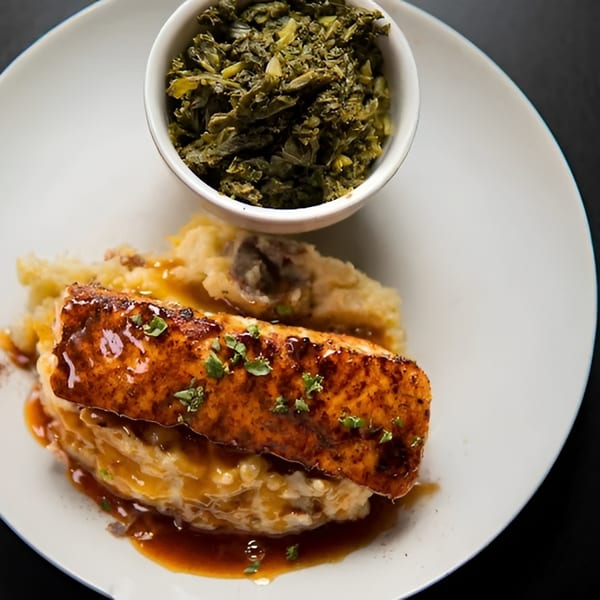 Glazed salmon fillet on mashed potatoes with a side of collard greens on a white plate.